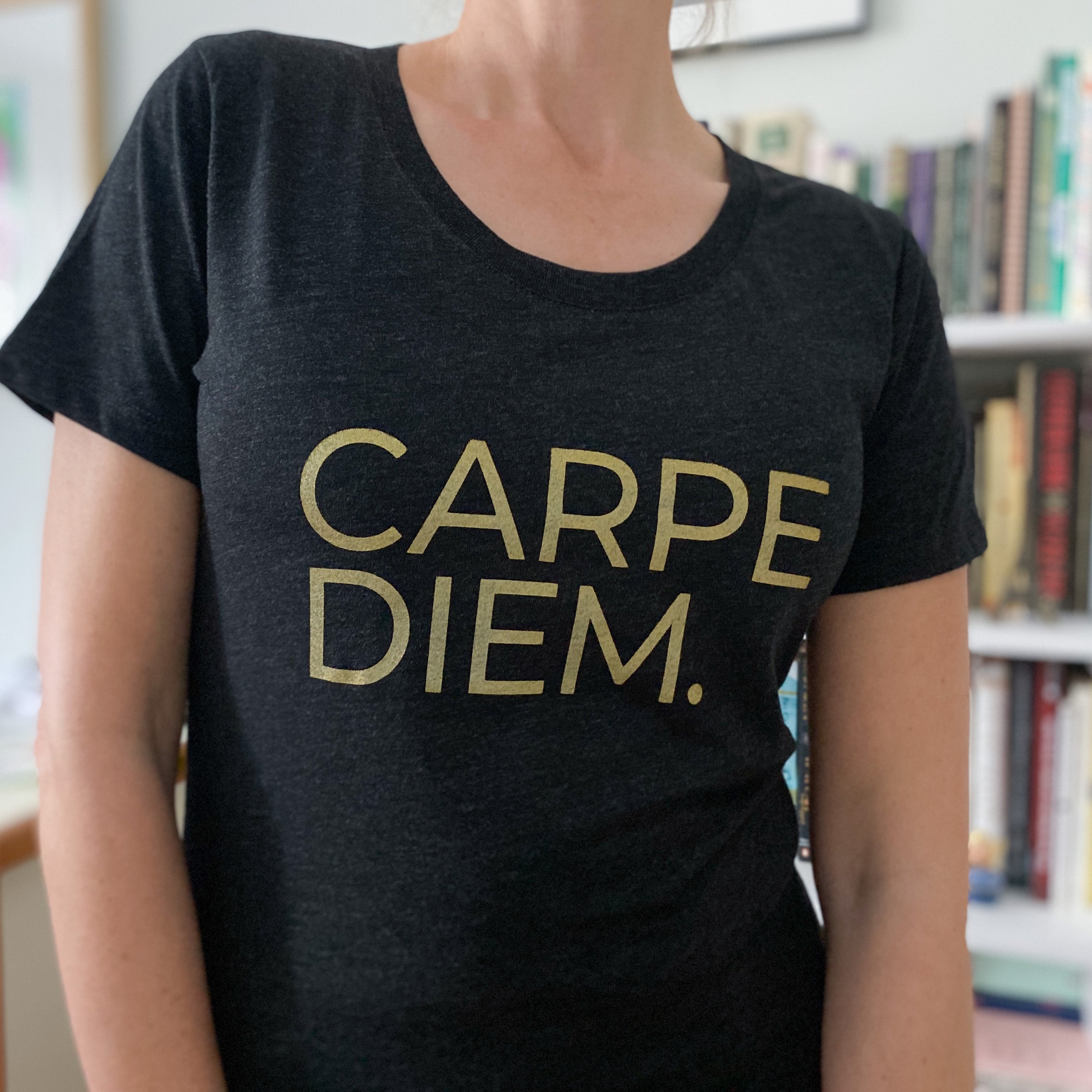 A picture of a woman wearing a charcoal black short-sleeved t-shirt with the words Carpe Diem in gold uppercase lettering.