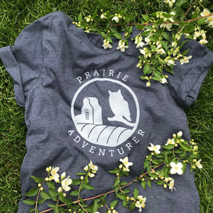 This navy t-shirt has silhouettes in white of a grain elevator on the left and a Great Horned Owl on the right. The curve of a hay bail appears at the bottom of the graphic.