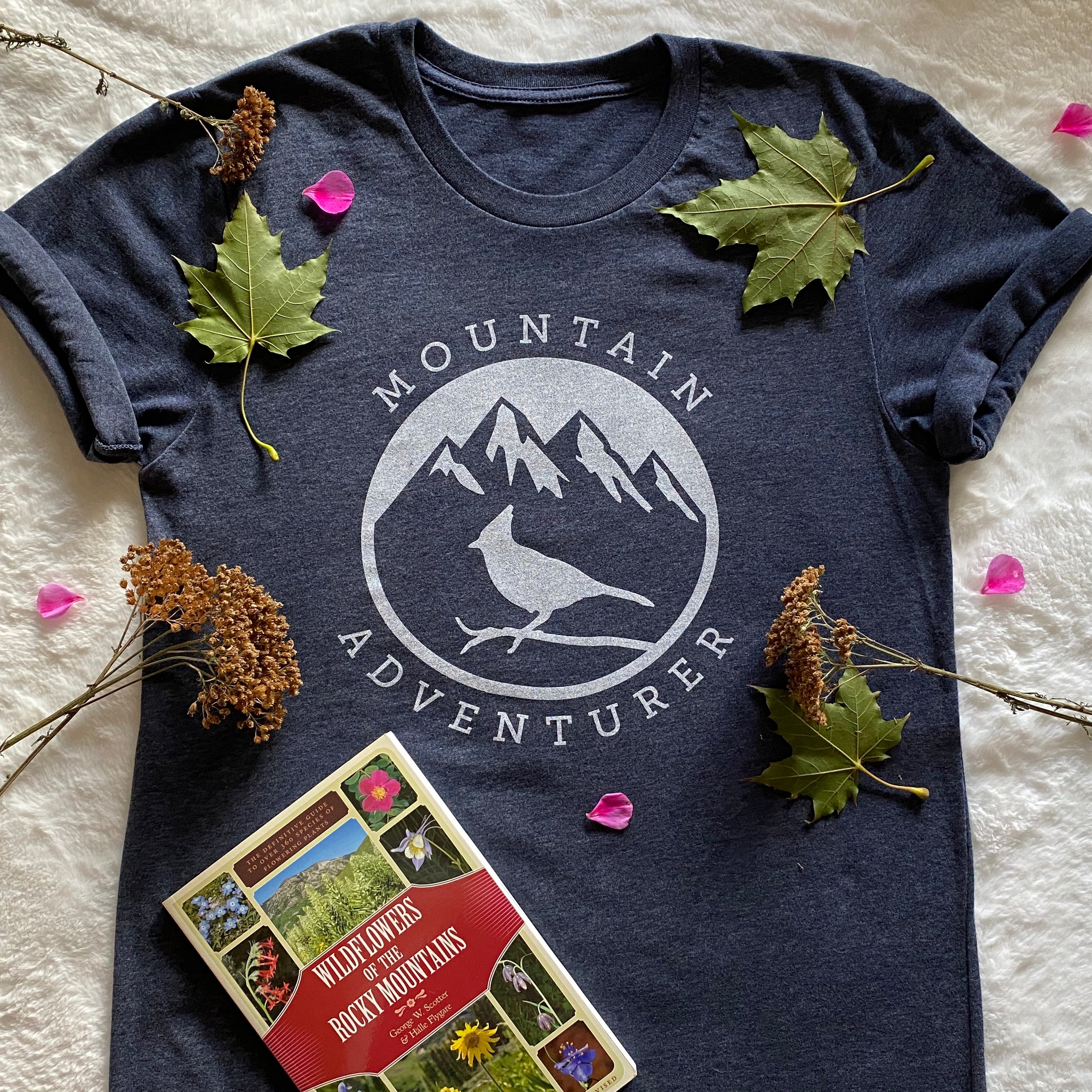 This navy t-shirt has a white silhouette of a Steller's Jay bird perched on a branch against a backdrop of mountains with snowy peaks.