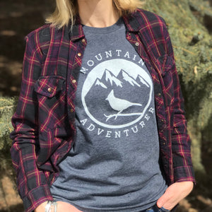 This navy t-shirt contains a white silhouette of a Steller's Jay perched on a branch against a backdrop of mountains with snowy peaks.  