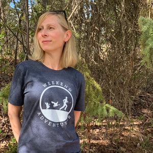A picture of a woman wearing the weekend adventurer tee.  This navy t-shirt has a white silhouette of a male golfer being chased by two Canadian geese.