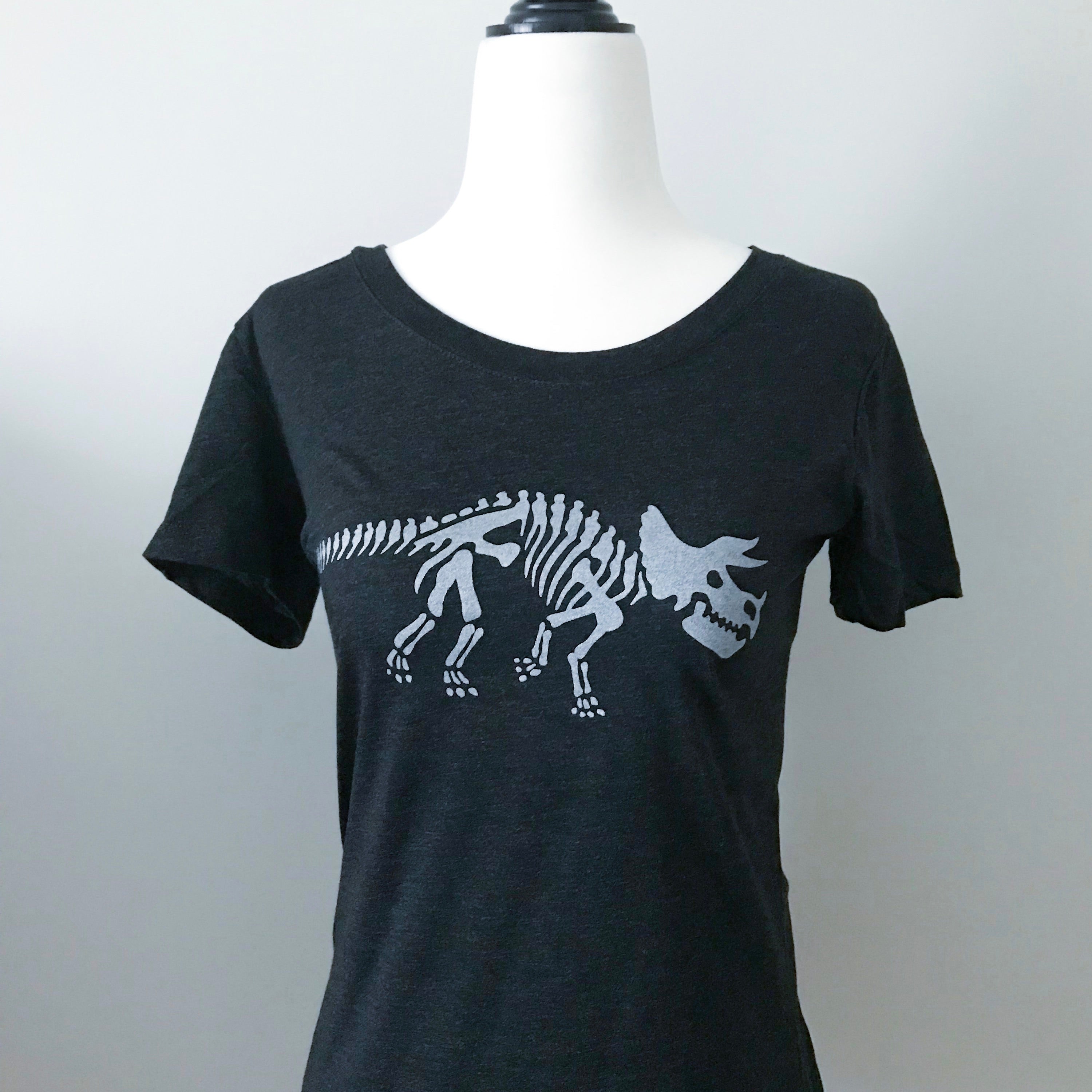 This short sleeved charcoal black t-shirt displays the skeleton of a triceratops dinosaur, printed in silver ink. 