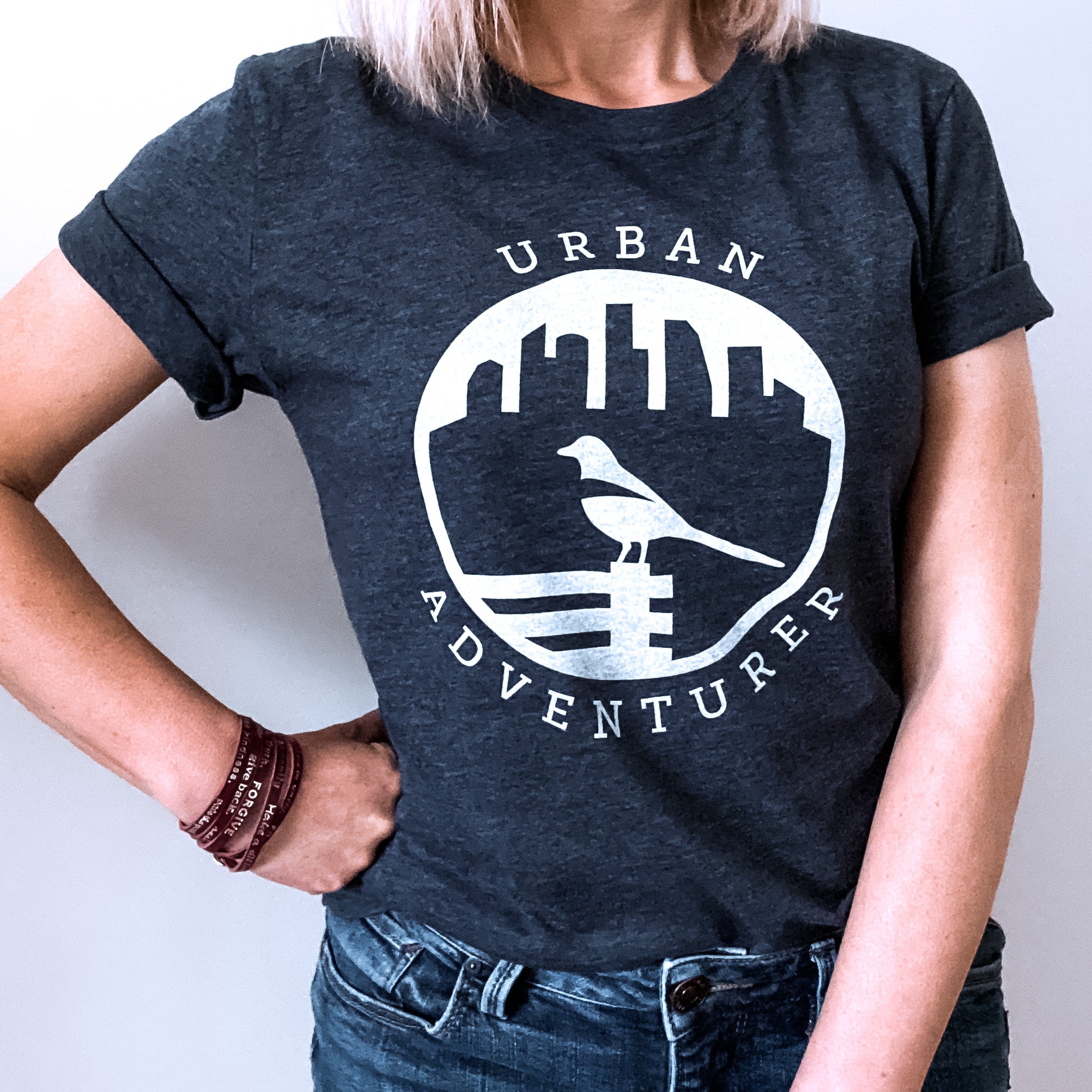This navy heather t-shirt contains a white silhouette of a magpie perched on a park bench.  In the background is a city skyline.