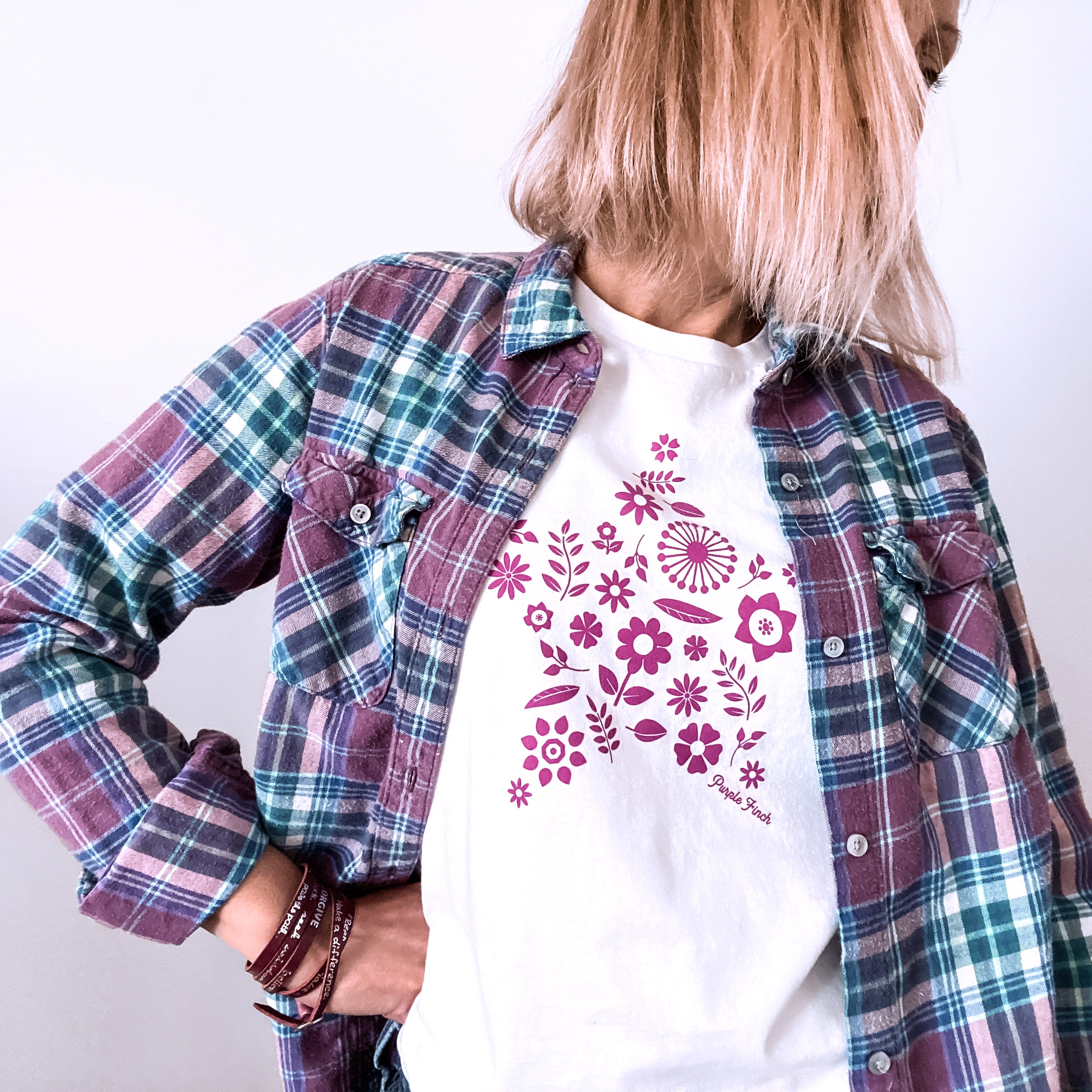 A picture of a woman wearing the star flower tee.  This white t-shirt has a magenta graphic print of a number of flowers and leaves grouped together into the shape of a star.