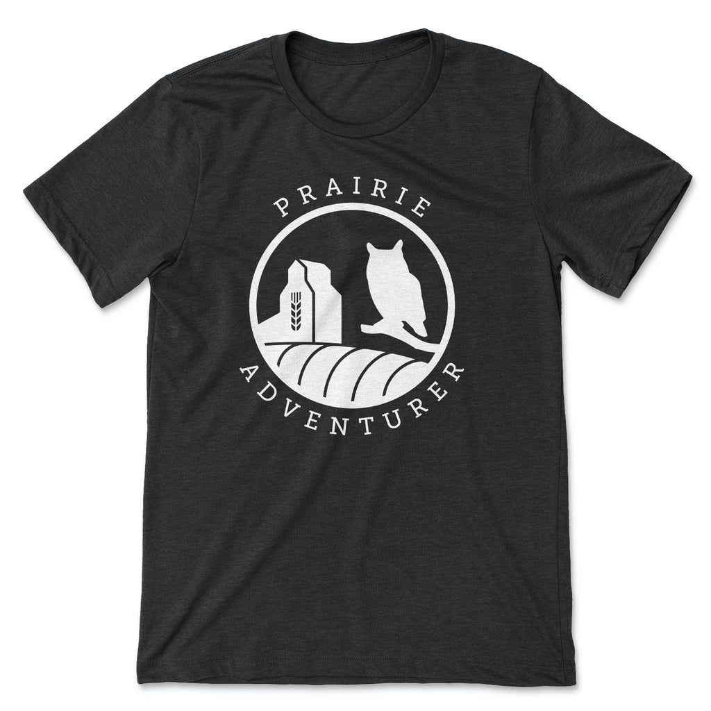 This black t-shirt has silhouettes in white of a grain elevator on the left and a Great Horned Owl on the right. The curve of a hay bail appears at the bottom of the graphic.